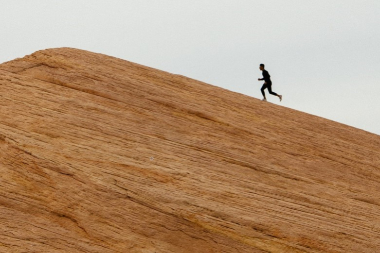 A person runs up a sand dune.
