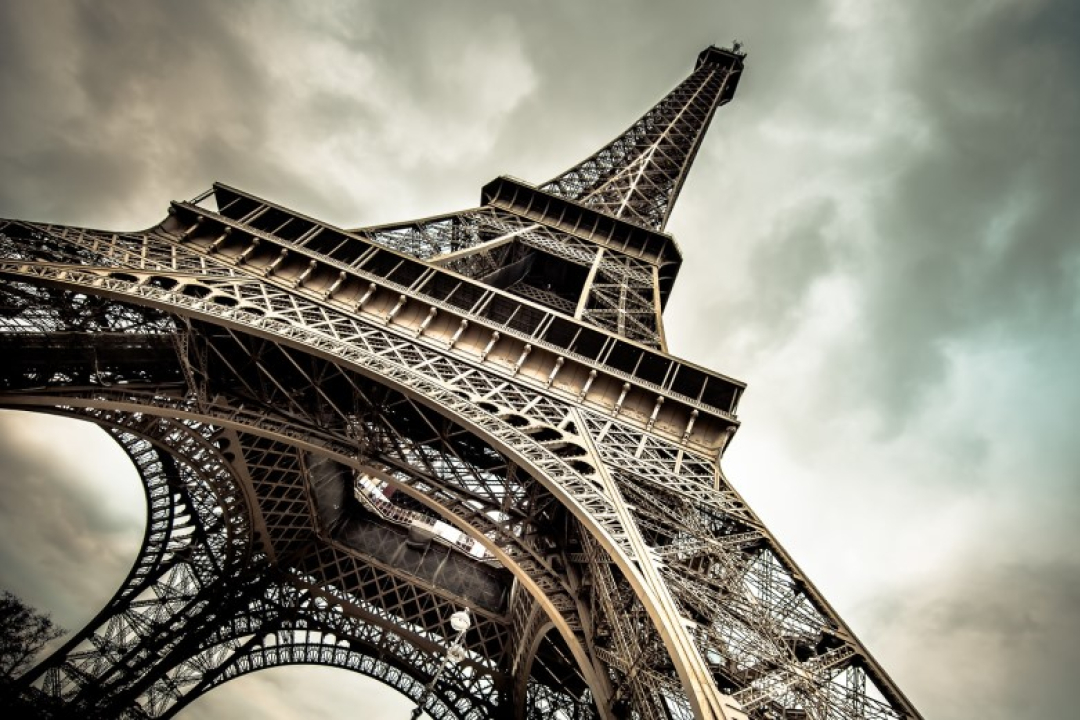 Low-angle view of the Eiffel Tower rising dramatically against a cloudy sky.
