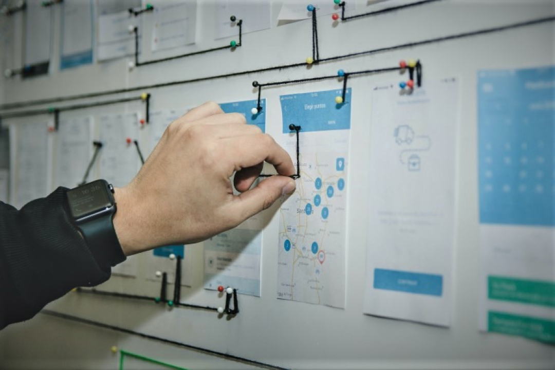 Close-up of a person’s hand arranging or connecting interface design mockups and workflow diagrams pinned to a wall.