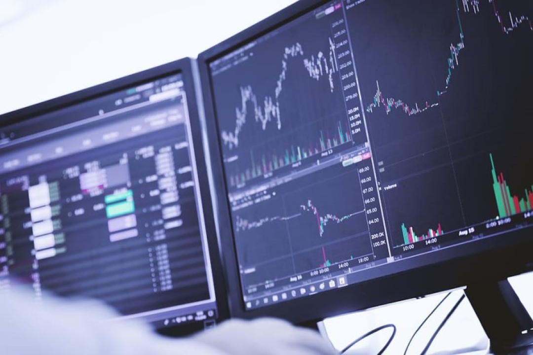 Multiple computer monitors display financial trading charts, stock market data, and price graphs in a professional trading or analytics environment.