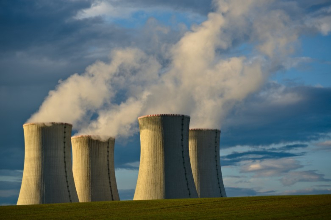 Large cooling towers release thick white steam into the sky at an industrial power plant, symbolizing energy production and heavy industry.
