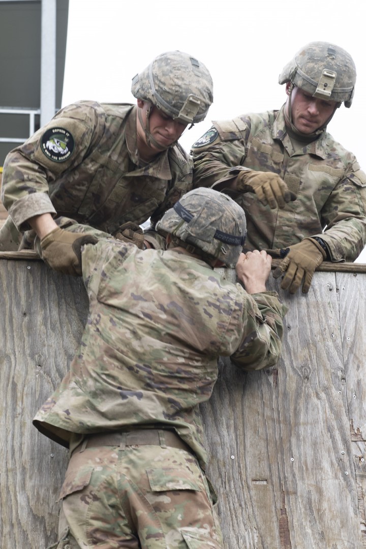 Two cadets help another over a wall.