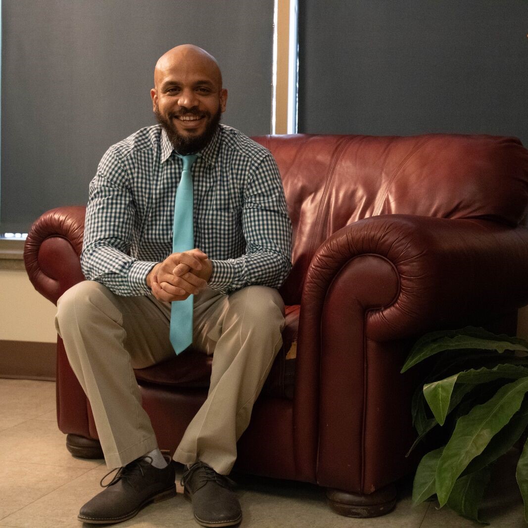 A man smiles as he sits on a couch.