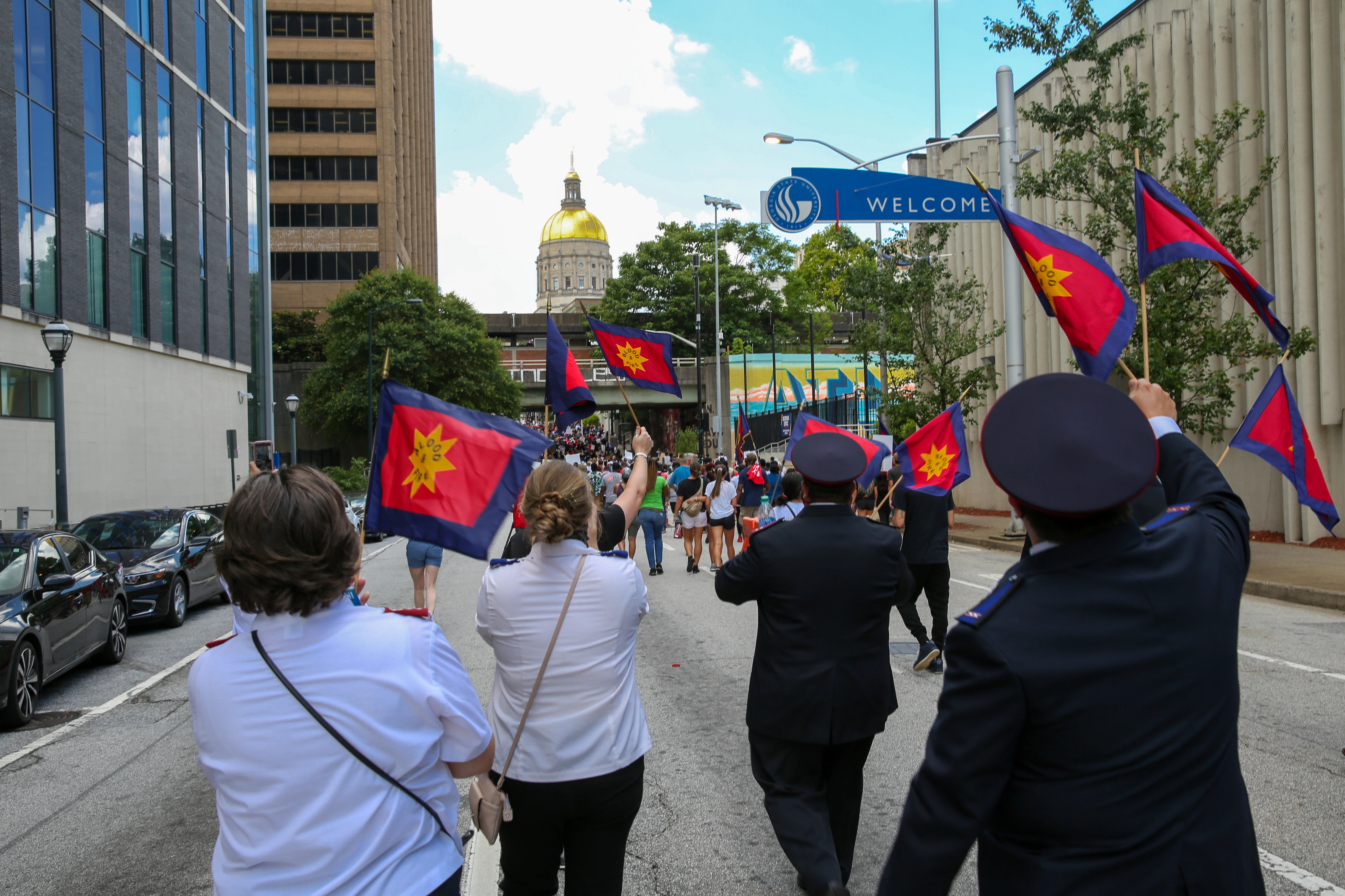 Salvation Army officers in uniform march along a city street carrying Army flags.