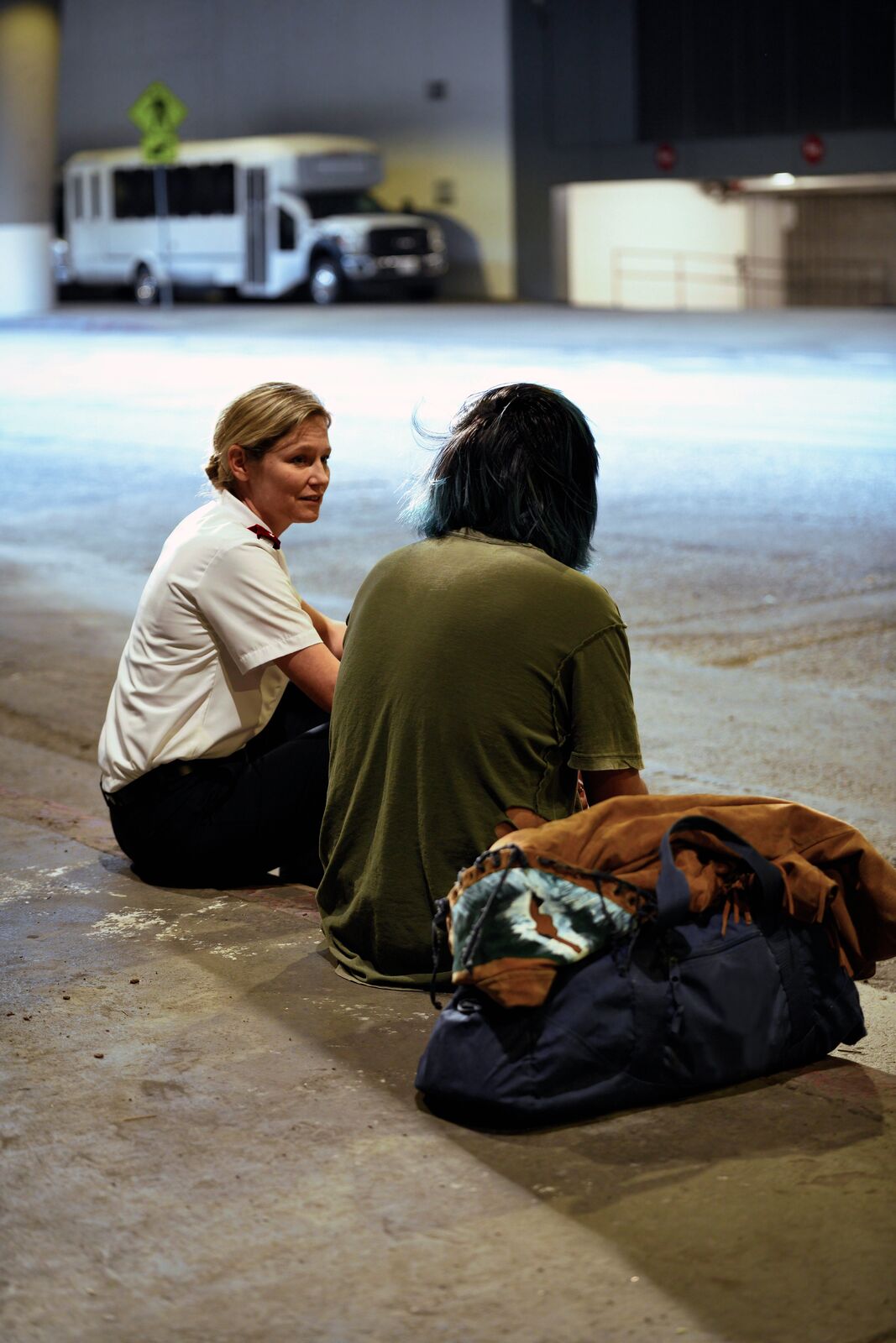 A Salvation Army officer sits on the pavement beside a person and their belongings, talking with them.