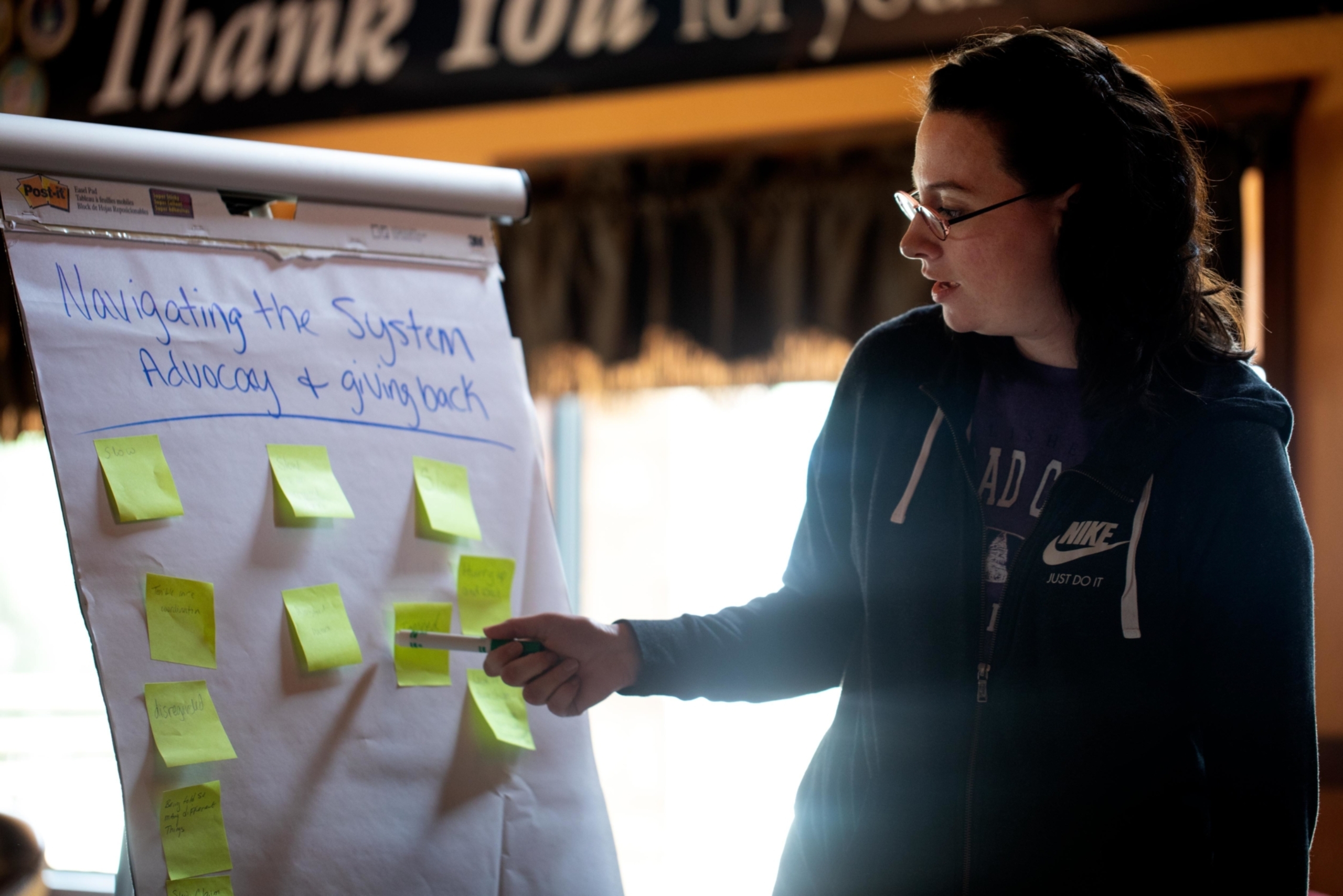 A woman appears before a poster with sticky notes attached.