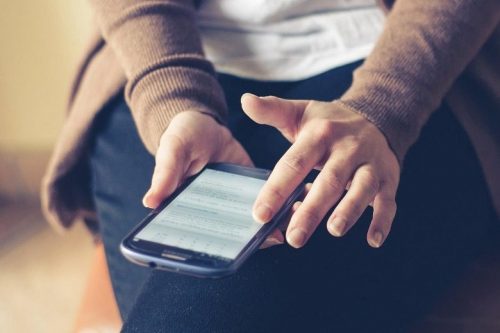 A woman sits while scrolling through her smartphone.