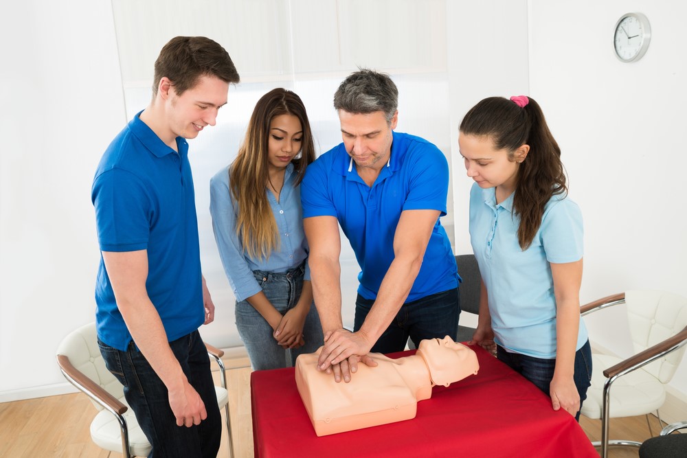 Instructor teaches three students CPR on a dummy.