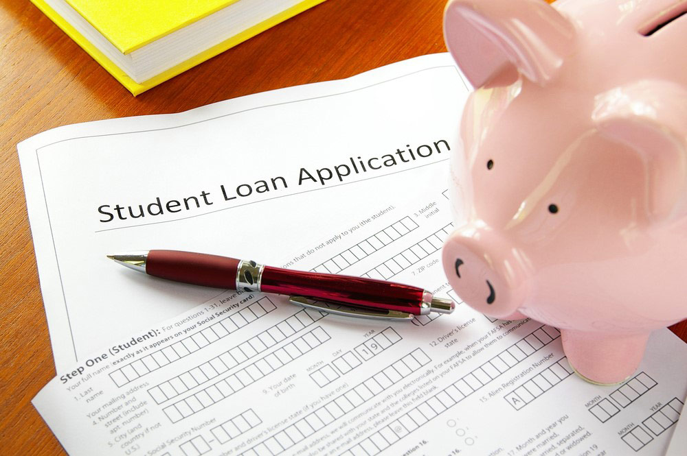 A student loan application sits on a table with a pink piggy bank and a red pen.