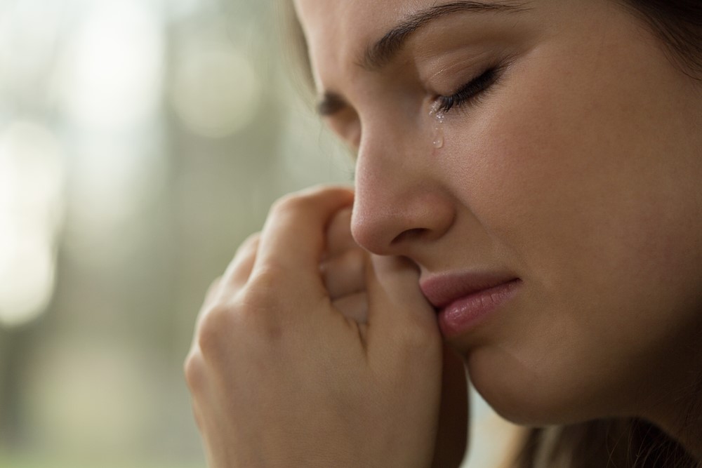Woman crying clutching clasped hands to cheek.