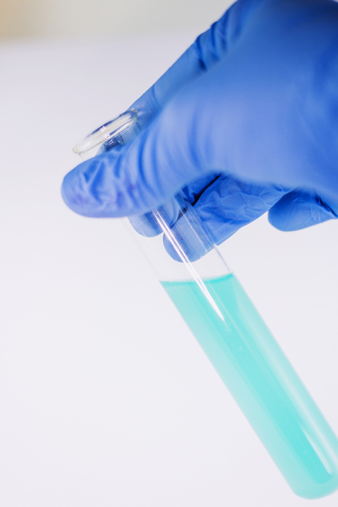 A gloved hand holding a small beaker filled with liquid.