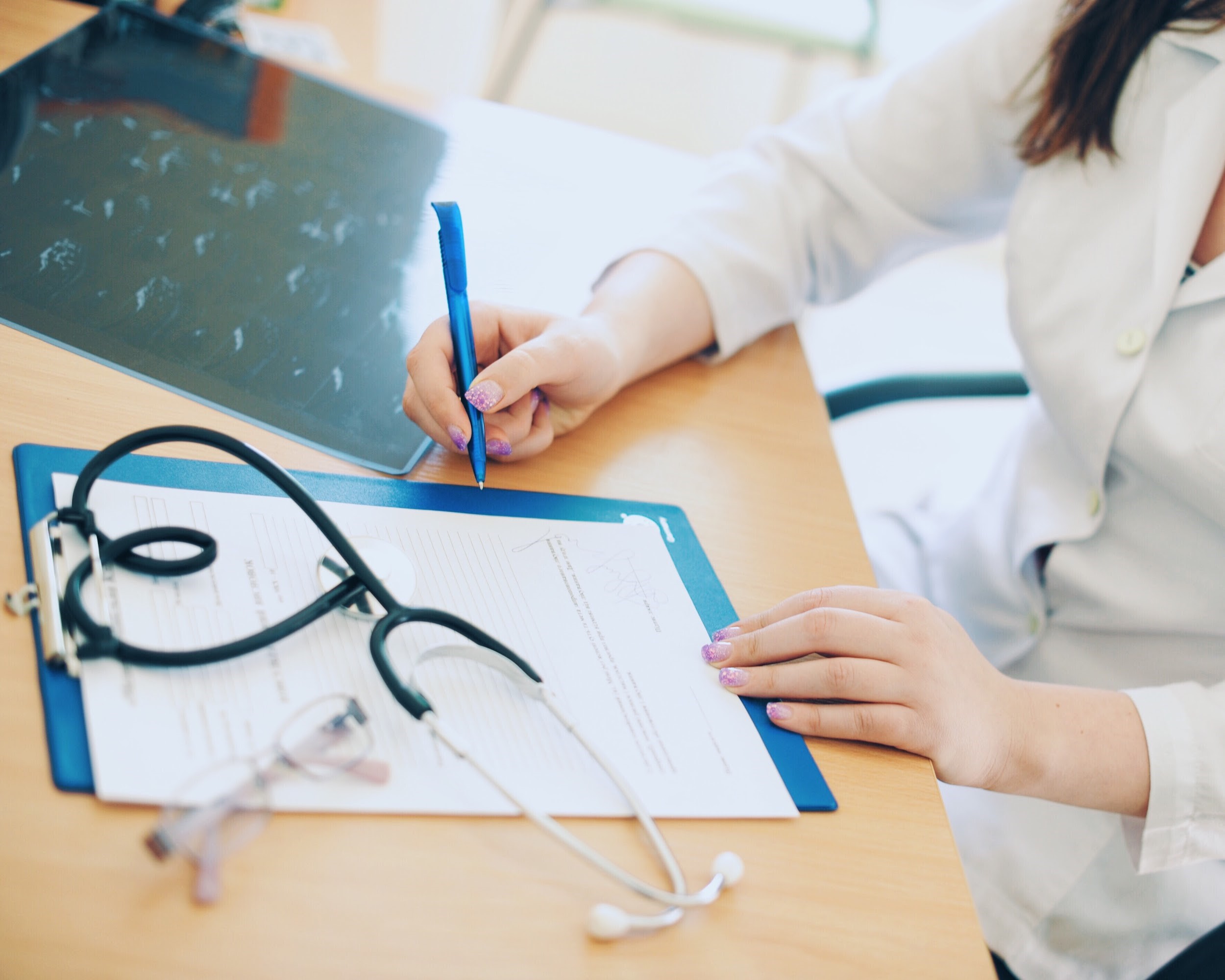 A nurse writes on a chart at an office desk.