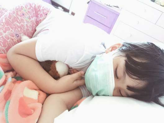 Young girl wearing flu mask while sleeping in bed