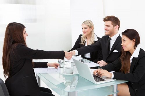 A man, sitting next to two women colleagues, shaking the hand of a job applicant.