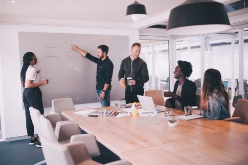 A group of people discuss information on a whiteboard.