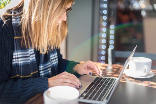 woman with glasses working on laptop at coffee shop with latte.