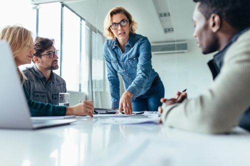 Several businesspeople listen to another who leads a meeting