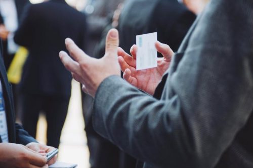 A businessman holding a business card while having a discussion with another person.