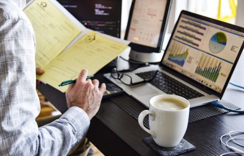 Person sitting at a desk holding a folder in front of a laptop with a cup of coffee. 