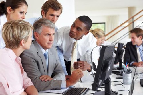 Businessmen and women in office huddled around desk looking at a computer monitor