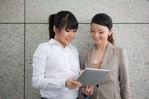 Two businesswomen standing outside using a tablet.