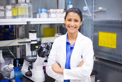 Young female smiling doctor in a lab coat standing in front of laboratory equipment