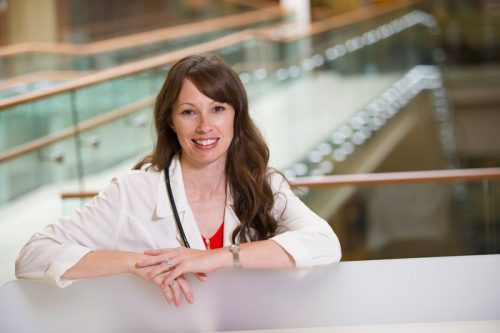Female Nurse With Long Brown Hair in a White Coat Smiling at the Camera