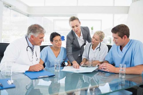 A group of male and female nurses and doctors consulting each other at the glass desk