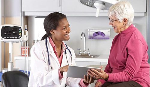 African American female doctor examining an elderly lady with grey hair in a red shirt