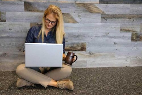 Young female with blond hair sitting on the floor with a laptop on her lap