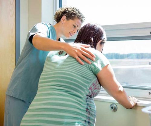 Female nurse holding her hand around elderly female patient in front of the window