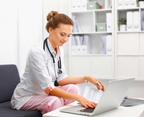Young female doctor with a stethoscope around the neck sitting in front of her laptop