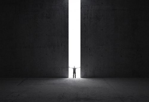 Human silhouette in distance against the light at the end of a dark room