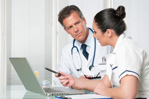 Female and male doctor sitting and talking in front of a laptop