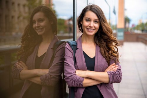 Female Counselor With Long Brown Hair Standing Outside Next to the Glass Wall and Smiling to the Camera
