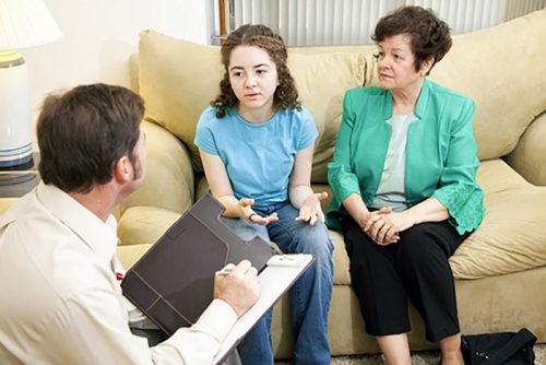 Elderly lady and her grandchild with long curly hair talking to the counselor writing down notes