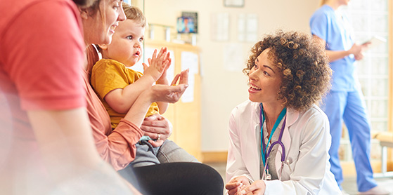 Female Nurse Practitioner Standing In Front of A Child in Yellow Shirt on Mother's Lap