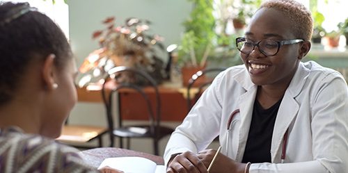Young Black female doctor sits at a desk with a patient and fills out a form