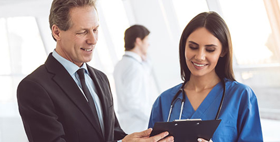 Older man in suit reviews clipboard with younger nurse