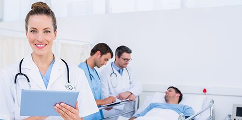 Female NP holding clipboard while patient is in bed in the background