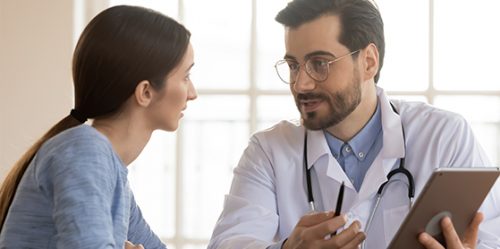 Male doctor with glasses speaks to female patient at a desk