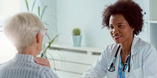 Young female African American doctor sits at desk and consults with gray-haired female patient