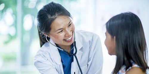 Female nurse practitioner uses stethoscope on adolescent patient in primary care office