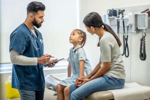 : A nurse practitioner with a parent and child in an examination room.