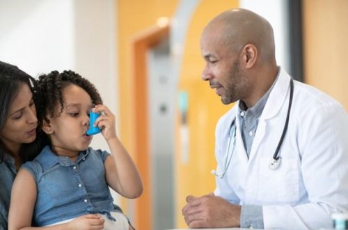 A family nurse practitioner shows a young patient how to use an inhaler.