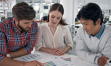 Two male and one female data scientists analyzing data from charts while sitting at the desk