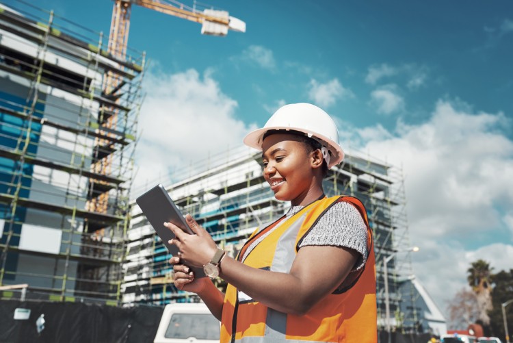 A person wearing a hard hat and reflective vest using a tablet at a construction site.