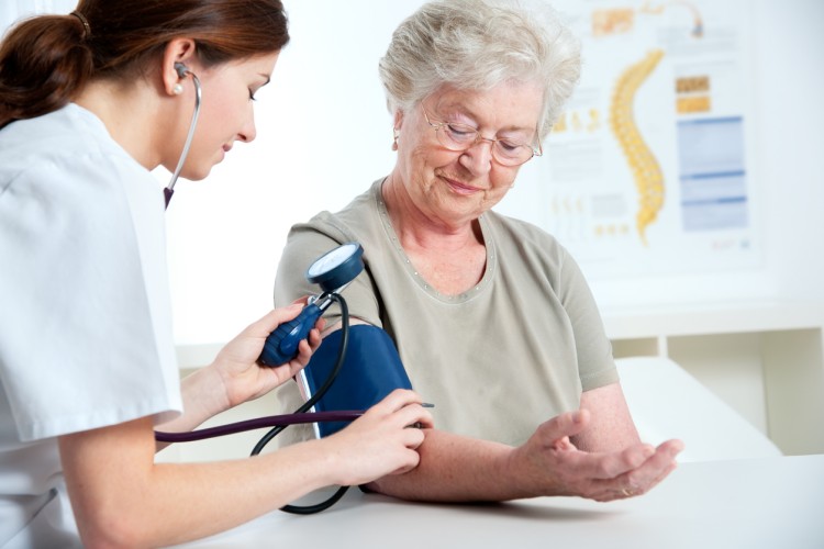 A nurse checks the blood pressure of a smiling older patient.