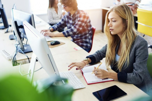 Online student writing in notebook and working on desktop