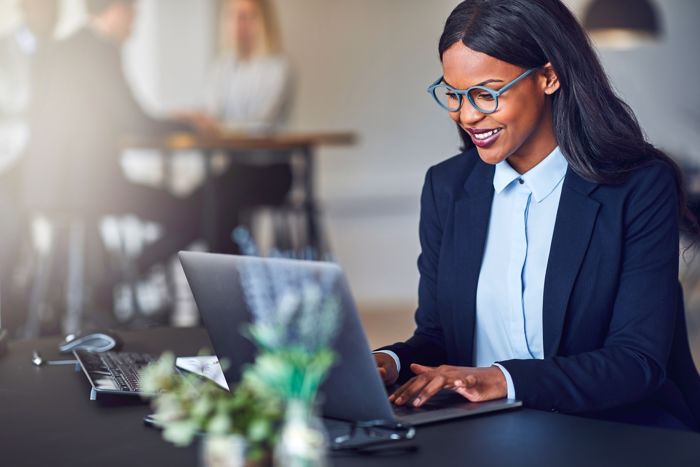 Woman in blue glasses smiling working on laptop.